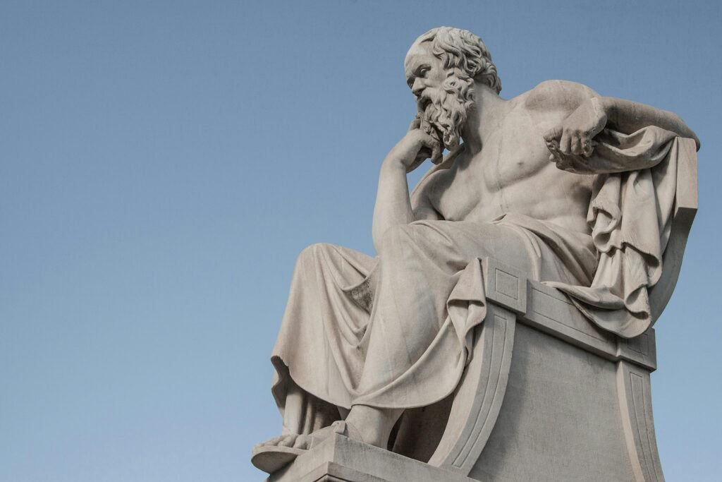 Stone statue of philosopher Socrates sitting in thoughtful pose in Athens, Greece under a clear blue sky.